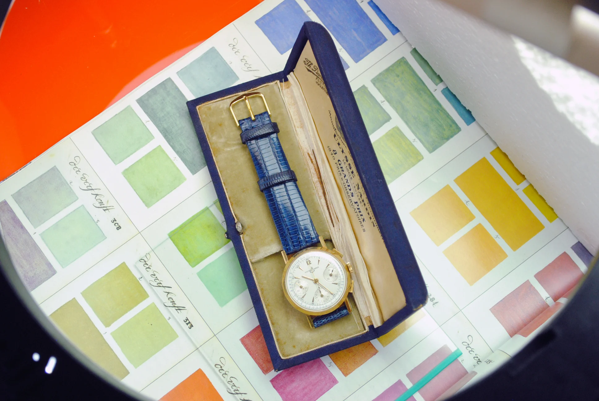 Sold Ulysse Nardin rose-gold chronograph displayed in its blue presentation box on a historic colour reference sheet