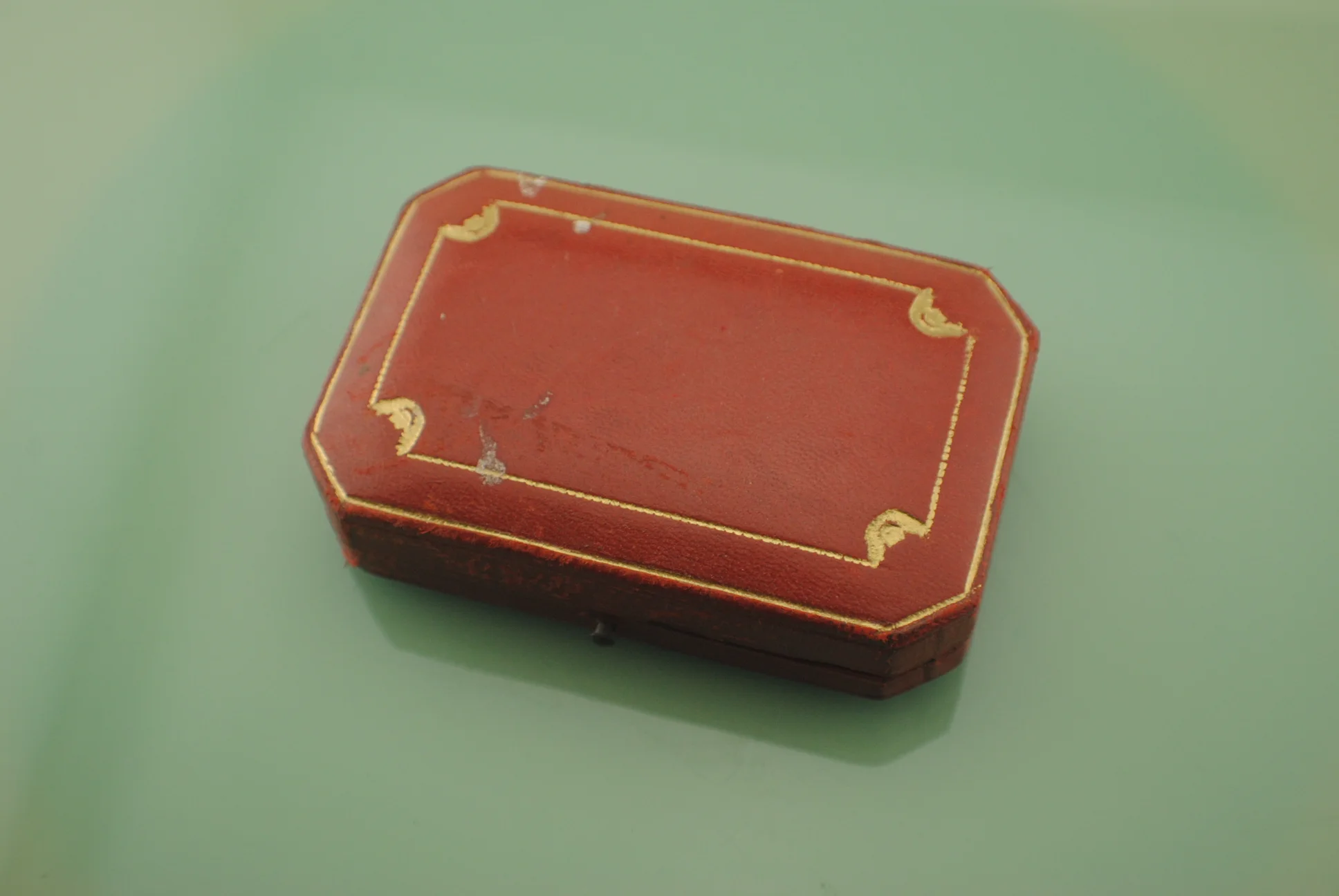 Closed red fitted Cartier presentation box with gold decorative border and corner details